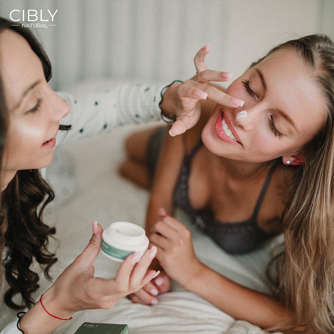 Жена нанася нощен крем Cibly Natural на лицето на приятелка, демонстрирайки нежната хидратация и грижата за кожата.